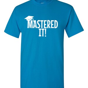 K&ouml;nnte beinhalten: T&uuml;rkisblaues T-Shirt mit dem wei&szlig;en Schriftzug "MASTERED IT!" und einer wei&szlig;en Abschlusskappe. Das T-Shirt hat einen Rundhalsausschnitt und kurze &Auml;rmel.