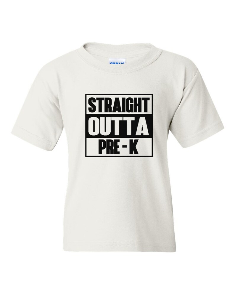 May include: A white t-shirt with the text "STRAIGHT OUTTA PRE-K" in a black box. The shirt is short-sleeved and appears to be made of cotton. The text is centered on the front of the shirt.