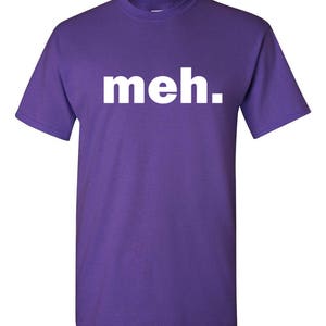 May include: A purple t-shirt with the word "meh." printed in white block letters across the chest. The shirt has short sleeves and a crew neck. The fabric appears to be a soft cotton blend.
