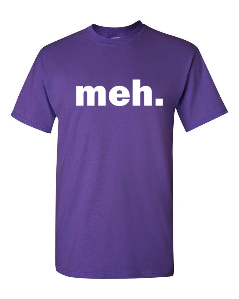 May include: A purple t-shirt with the word "meh." printed in white block letters across the chest. The shirt has short sleeves and a crew neck. The fabric appears to be a soft cotton blend.