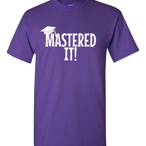 K&ouml;nnte beinhalten: Ein lila T-Shirt mit dem wei&szlig;en Schriftzug "MASTERED IT!" und einer wei&szlig;en Abschlusskappe. Das T-Shirt hat einen Rundhalsausschnitt und kurze &Auml;rmel.