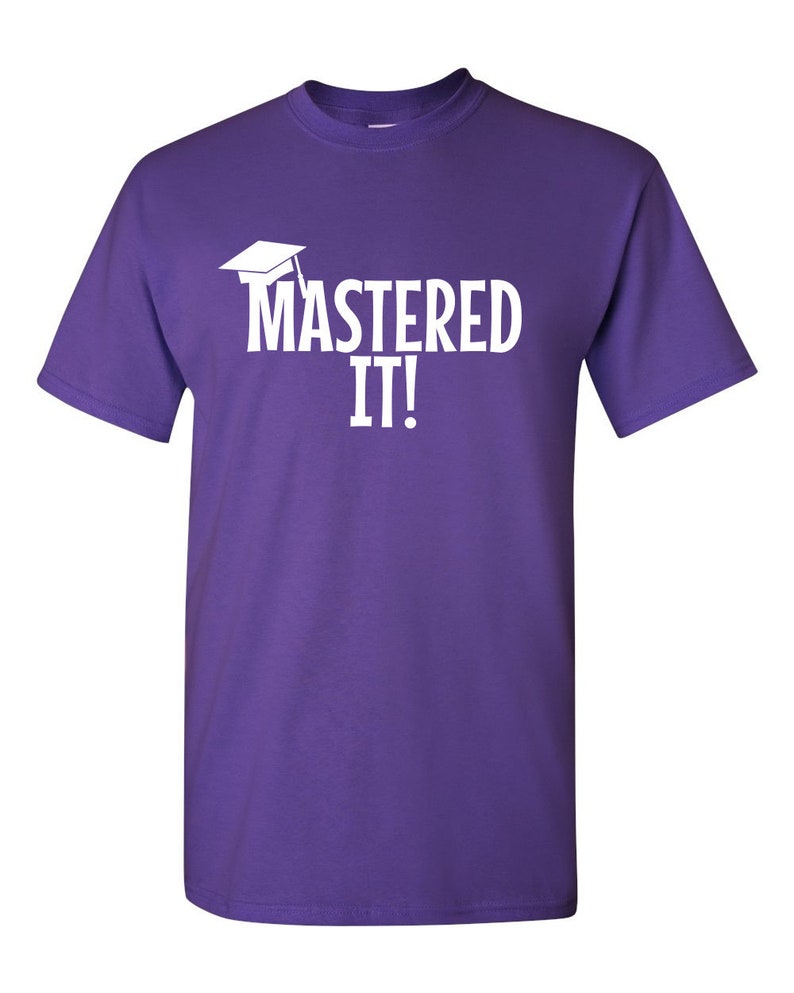K&ouml;nnte beinhalten: Ein lila T-Shirt mit dem wei&szlig;en Schriftzug "MASTERED IT!" und einer wei&szlig;en Abschlusskappe. Das T-Shirt hat einen Rundhalsausschnitt und kurze &Auml;rmel.