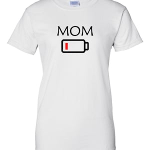 Pu&ograve; includere: T-shirt bianca con la scritta "MOM" in lettere maiuscole nere sopra un'icona di batteria nera con una barra rossa che indica batteria scarica. La maglietta &egrave; a girocollo.