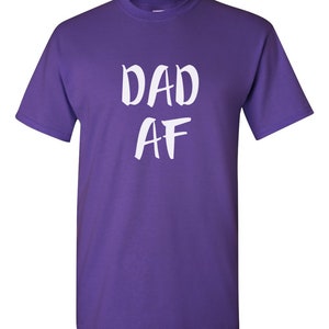 Peut inclure: Un t-shirt violet avec le texte blanc "DAD AF" &eacute;crit &agrave; la main. Le t-shirt a des manches courtes et un col rond.
