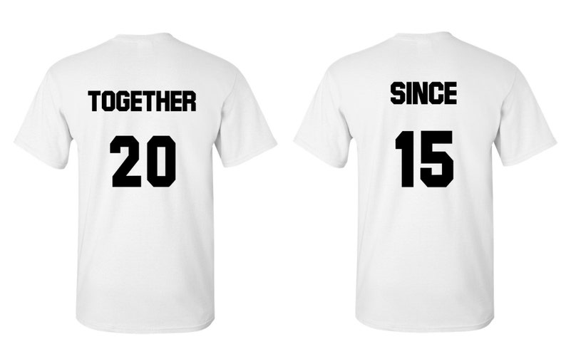 Op de afbeelding: Twee witte T-shirts met zwarte tekst. Het eerste shirt zegt "TOGETHER 20" en het tweede shirt zegt "SINCE 15".
