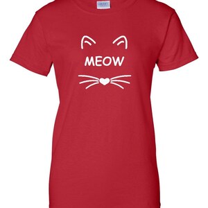 Puede incluir: Camiseta roja con un dise&ntilde;o de cara de gato blanco. El dise&ntilde;o incluye orejas de gato, la palabra "MEOW" y bigotes con una nariz en forma de coraz&oacute;n. La camiseta est&aacute; hecha de un material suave.