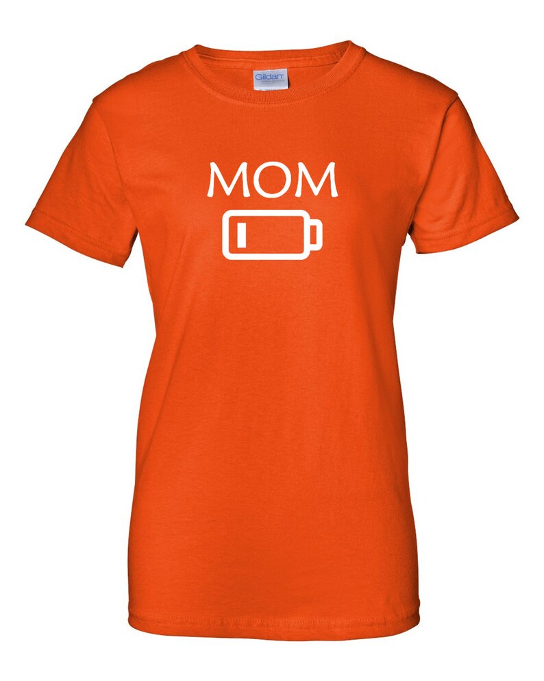 Pu&ograve; includere: T-shirt arancione con la scritta "MOM" in lettere maiuscole bianche sopra un'icona di batteria bianca con un indicatore di batteria scarica. La maglietta &egrave; in materiale morbido e ha maniche corte.