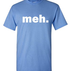 May include: Light blue t-shirt with the word "meh." printed in white block letters. The shirt has short sleeves and a crew neck. The text is centered on the front of the shirt.