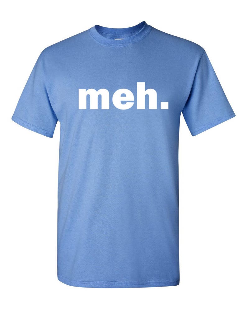 May include: Light blue t-shirt with the word "meh." printed in white block letters. The shirt has short sleeves and a crew neck. The text is centered on the front of the shirt.