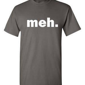 May include: A gray t-shirt with the word "meh." printed in white block letters. The shirt has short sleeves and a crew neck. The text is centered on the front of the shirt.