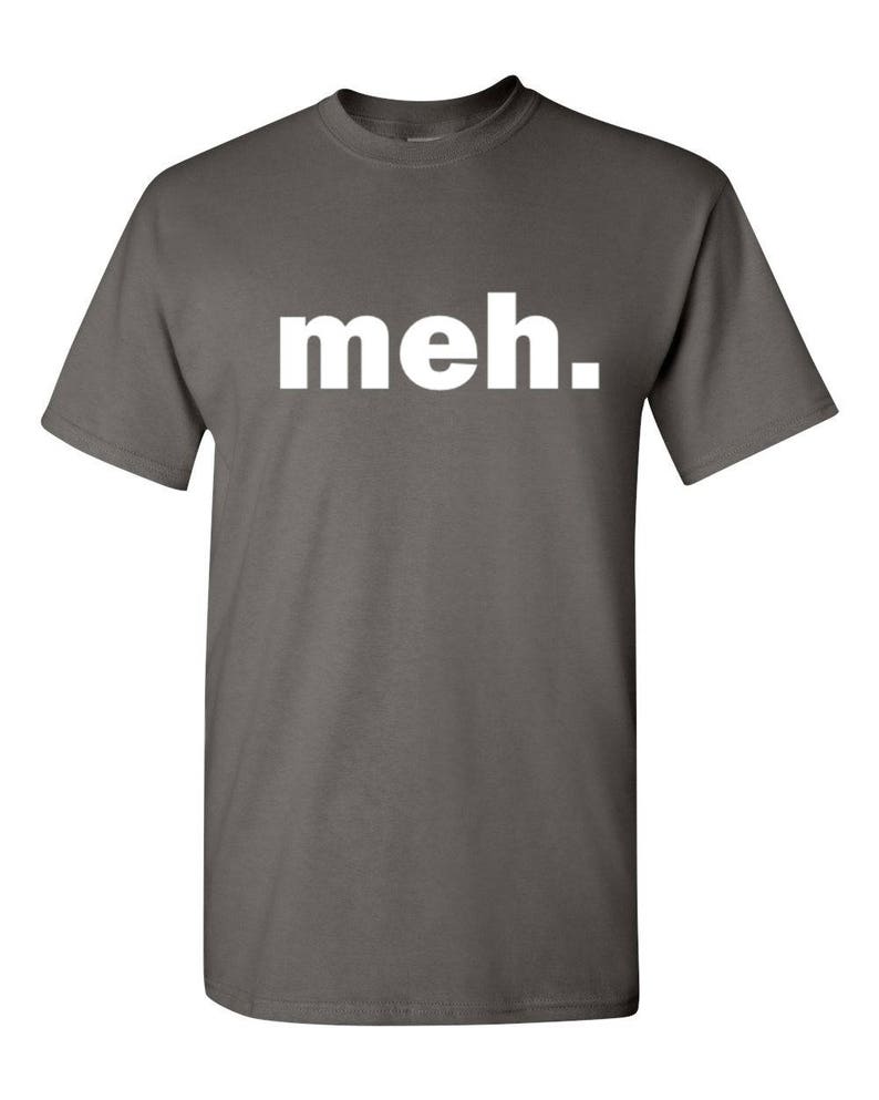 May include: A gray t-shirt with the word "meh." printed in white block letters. The shirt has short sleeves and a crew neck. The text is centered on the front of the shirt.