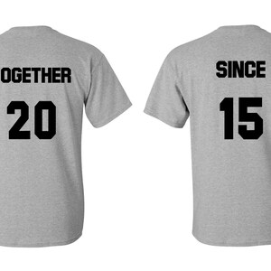Op de afbeelding: Twee grijze T-shirts met zwarte tekst. Het eerste shirt zegt "TOGETHER 20" en het tweede shirt zegt "SINCE 15".