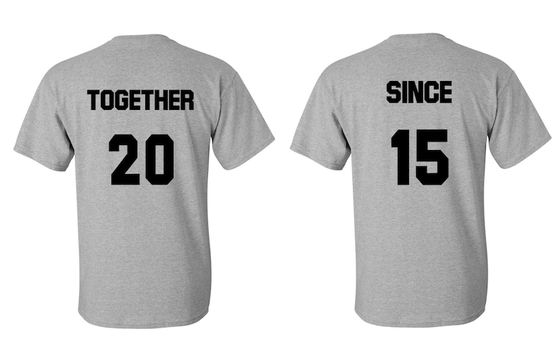 Op de afbeelding: Twee grijze T-shirts met zwarte tekst. Het eerste shirt zegt "TOGETHER 20" en het tweede shirt zegt "SINCE 15".