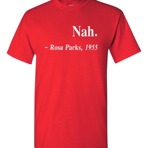 May include: A bright red t-shirt with the word "Nah." printed in white, followed by "- Rosa Parks, 1955." The shirt is a classic crew neck style, made of a soft material.