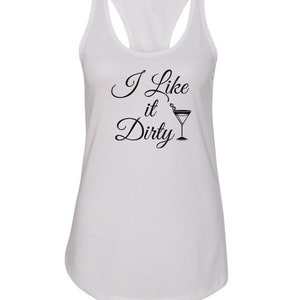 May include: White racerback tank top with the text "I Like it Dirty" in black script, accompanied by a martini glass illustration. The tank top has a scoop neck and a racerback design.
