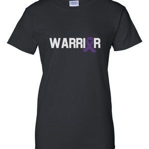 Puede incluir: Camiseta negra con la palabra "WARRIOR" en letras blancas y una cinta morada de concienciaci&oacute;n. La camiseta es de cuello redondo y est&aacute; hecha de un material suave. Corte cl&aacute;sico.