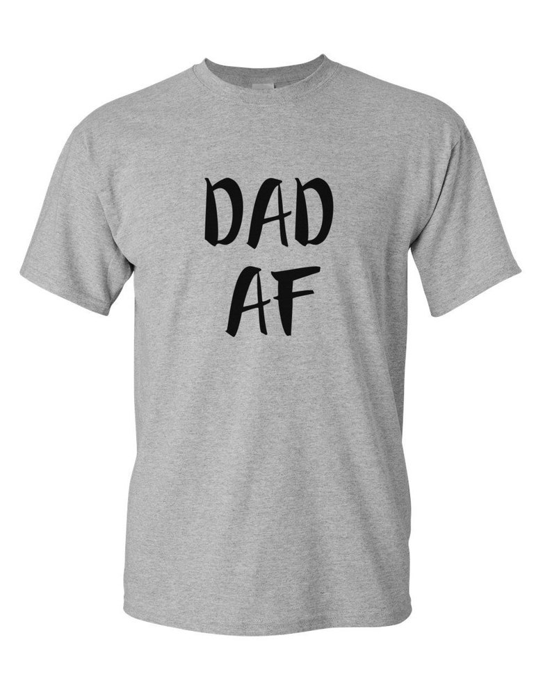 Peut inclure: Un t-shirt gris chin&eacute; avec l'inscription "DAD AF" en lettres noires grasses. Le t-shirt a des manches courtes et un col rond.
