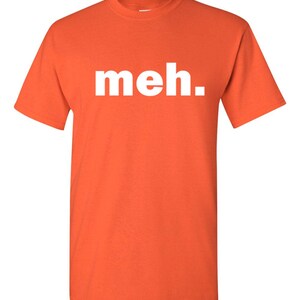 May include: Orange t-shirt with the word "meh." printed in white. The shirt has short sleeves and a crew neck. The text is centered on the front of the shirt.