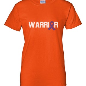 Puede incluir: Una camiseta naranja con la palabra "WARRIOR" en letras blancas. Una cinta morada de concienciaci&oacute;n sustituye a la letra "I". La camiseta es de un material suave y tiene mangas cortas.
