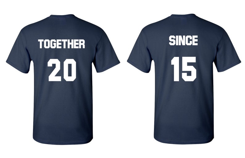Op de afbeelding: Twee donkerblauwe T-shirts met witte tekst. Het eerste shirt zegt "TOGETHER 20" en het tweede shirt zegt "SINCE 15".