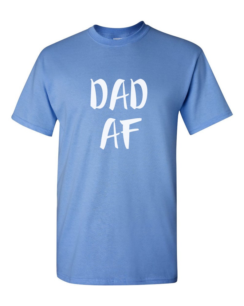 Peut inclure: Un t-shirt bleu clair avec le texte blanc "DAD AF" &eacute;crit &agrave; la main. Le t-shirt a des manches courtes et un col rond.