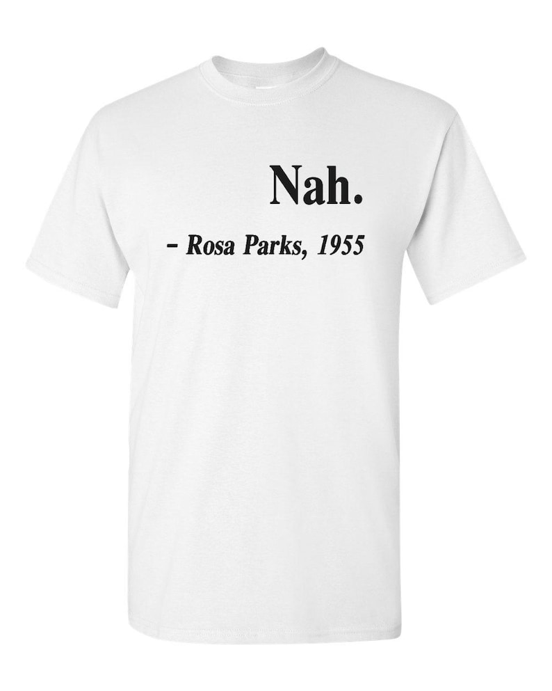 May include: White t-shirt with the word "Nah" in a bold, black font at the top center. Below the word is the text "- Rosa Parks, 1955" in a smaller, black font. The shirt is a classic crew neck style.