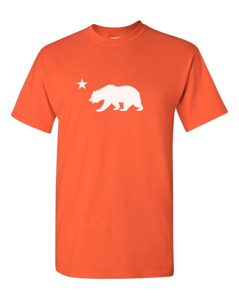May include: Orange short-sleeved t-shirt with a white silhouette of a bear and a star.