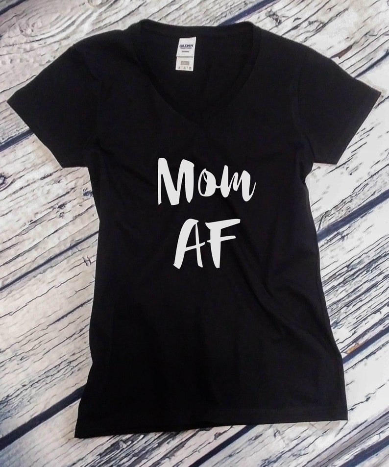May include: Black V-neck t-shirt with the white text "Mom AF". The shirt is made of a soft material. The Gildan brand tag is visible at the top of the shirt.