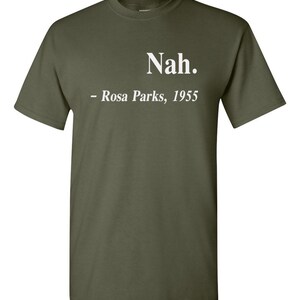 May include: Olive green t-shirt with the text "Nah." above "- Rosa Parks, 1955" in white. The shirt is a crew neck style and appears to be made of a soft material.
