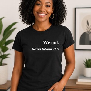 May include: A black short-sleeved t-shirt featuring white text printed on the chest that reads, "We out. - Harriet Tubman, 1849." The shirt has a classic crew neckline and a standard fit, constructed from a solid black fabric with crisp white lettering.