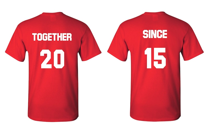 Op de afbeelding: Twee rode T-shirts met witte tekst. Het eerste shirt zegt "TOGETHER 20" en het tweede shirt zegt "SINCE 15".