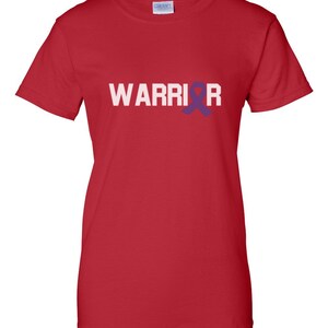 Puede incluir: Camiseta roja con la palabra "WARRIOR" en letras blancas. Una cinta morada reemplaza la letra "O". La camiseta est&aacute; hecha de un material suave y tiene mangas cortas.