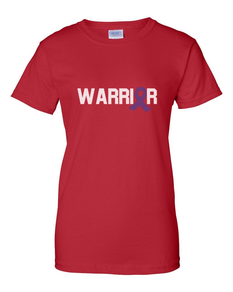 Puede incluir: Camiseta roja con la palabra "WARRIOR" en letras blancas. Una cinta morada reemplaza la letra "O". La camiseta est&aacute; hecha de un material suave y tiene mangas cortas.