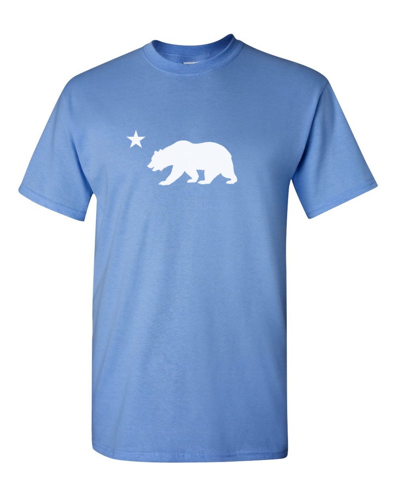 May include: A light blue t-shirt with a white silhouette of a bear and a star.