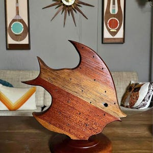 May include: A wooden fish-shaped earring holder with a stand. The holder is made of multiple types of wood, including mahogany and walnut. The holder has a natural wood finish and is decorated with small holes for earrings.