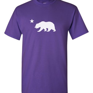 May include: Purple short-sleeved t-shirt with a white silhouette of a bear and a star.