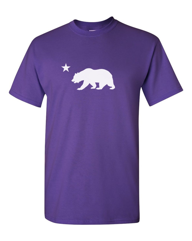 May include: Purple short-sleeved t-shirt with a white silhouette of a bear and a star.