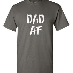 Peut inclure: Un t-shirt gris anthracite avec l'inscription blanche "DAD AF" imprim&eacute;e sur le devant. Le t-shirt a un col rond et des manches courtes. Le texte est &eacute;crit dans un style manuscrit audacieux.
