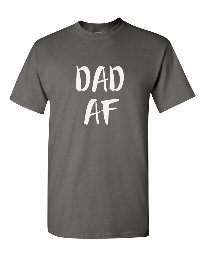 Peut inclure: Un t-shirt gris anthracite avec l'inscription blanche "DAD AF" imprim&eacute;e sur le devant. Le t-shirt a un col rond et des manches courtes. Le texte est &eacute;crit dans un style manuscrit audacieux.