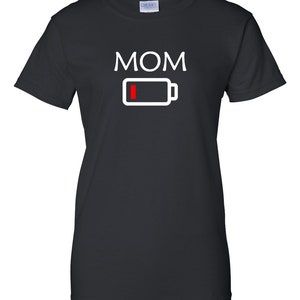 Pu&ograve; includere: T-shirt nera con la scritta "MOM" in lettere maiuscole bianche sopra un'icona di batteria bianca con una barra rossa che indica batteria scarica. Girocollo.