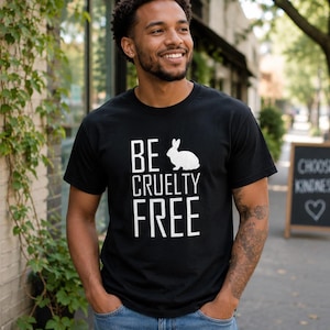 K&ouml;nnte beinhalten: Ein schwarzes kurz&auml;rmeliges T-Shirt mit wei&szlig;em Aufdruck BE CRUELTY FREE und einer Kaninchensilhouette zwischen den W&ouml;rtern BE und CRUELTY. Das Shirt hat einen Rundhalsausschnitt und eine normale Passform aus Baumwollstoff.