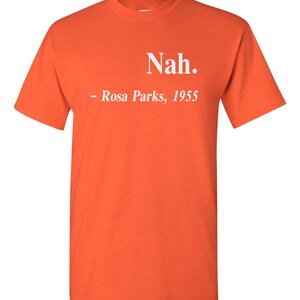 May include: Bright orange t-shirt with the text "Nah." and "- Rosa Parks, 1955" printed in white. The shirt is a short-sleeved crew neck style.