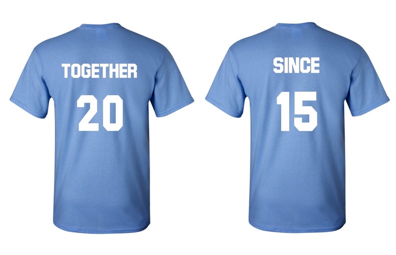 Op de afbeelding: Twee lichtblauwe T-shirts met witte tekst. Het linker T-shirt zegt "TOGETHER 20" en het rechter T-shirt zegt "SINCE 15".
