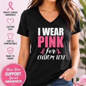 May include: Black V-neck t-shirt with the text "I WEAR PINK for CUSTOM TEXT" in white and pink. The shirt promotes breast cancer awareness. The image also includes pink ribbons and the words "Personalized" and "Show Your SUPPORT Spread AWARENESS".