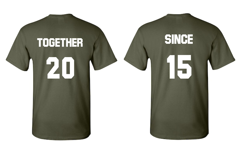Op de afbeelding: Twee olijfgroene T-shirts met witte tekst. Het eerste shirt zegt "TOGETHER 20" en het tweede shirt zegt "SINCE 15".