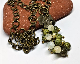 May include: A vintage necklace with a bronze chain and a cluster of green and white beads. The pendant features a bronze leaf and small pearls. The necklace is displayed on a reddish-brown stone.