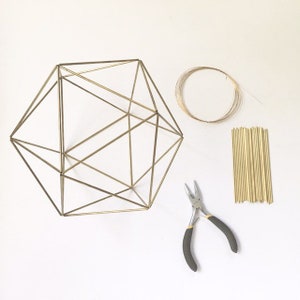 May include: A gold geometric wire frame with a set of gold wire pieces, a spool of gold wire, and a pair of pliers.