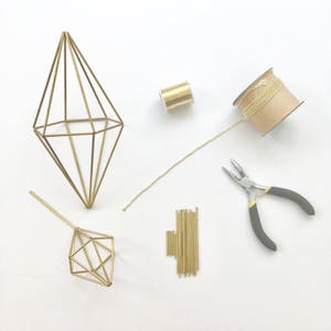 May include: A gold geometric wire frame, a spool of gold wire, a chain, a pair of pliers, and a bundle of gold metal rods on a white surface.