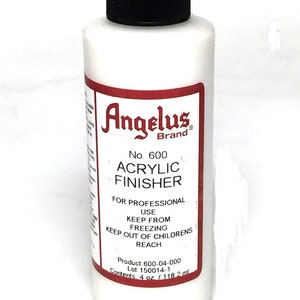 May include: A white bottle of Angelus Brand No. 600 Acrylic Finisher for professional use. The bottle has a black cap and a red label with white text. The label says "Keep from freezing. Keep out of children's reach. Product 600-04-000. Lot 150014-1. Contents: 4 oz. / 118.2 ml."