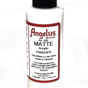 May include: A 4-ounce bottle of Angelus Brand Matte Acrylic Finisher. The bottle is white with a red label that says "Angelus Brand" and "Matte Acrylic Finisher". The label also includes the product number 620, instructions for use, and the product's lot number.